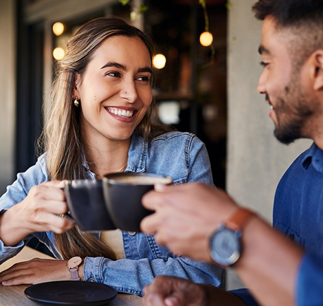 A man and woman sitting together at a coffee shop and holding mugs.
