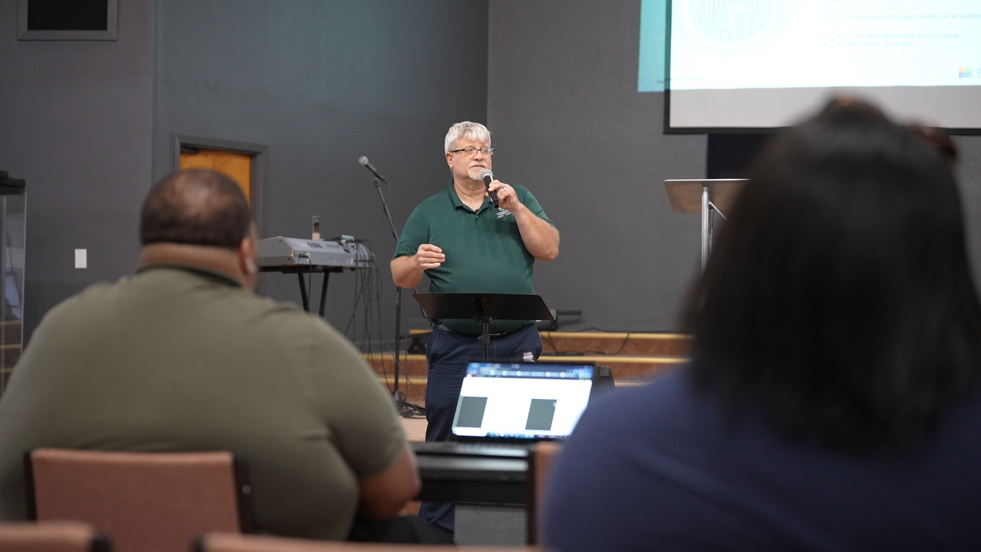 A speaker talking in front of people at a public event.
