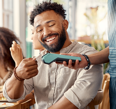 A man sitting down and making a contactless payment.
