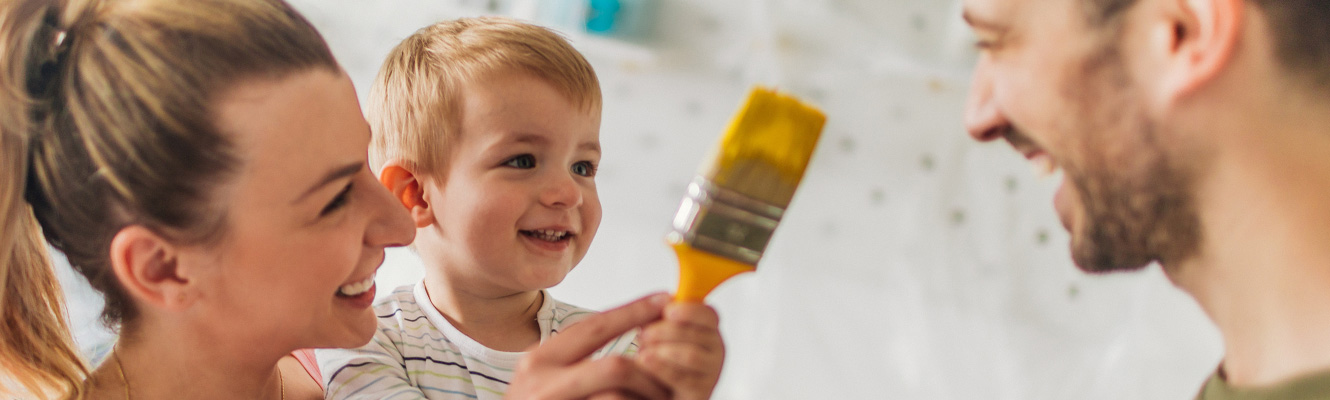 Mother and father helping their child hold a paintbrush.
