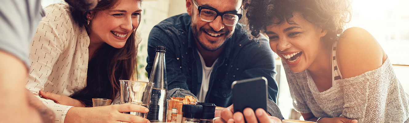 A group of people leaning over next to each other, looking at a phone.
